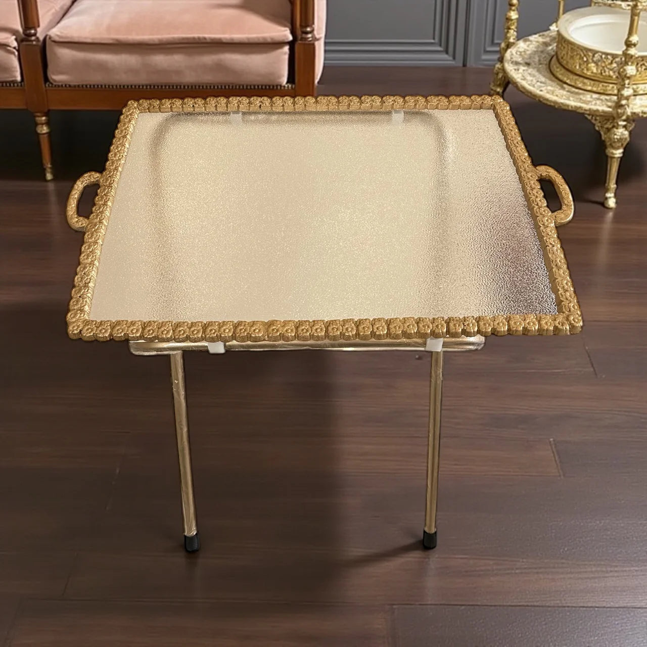 Decorative tray with gold frame and handles on a wooden floor.